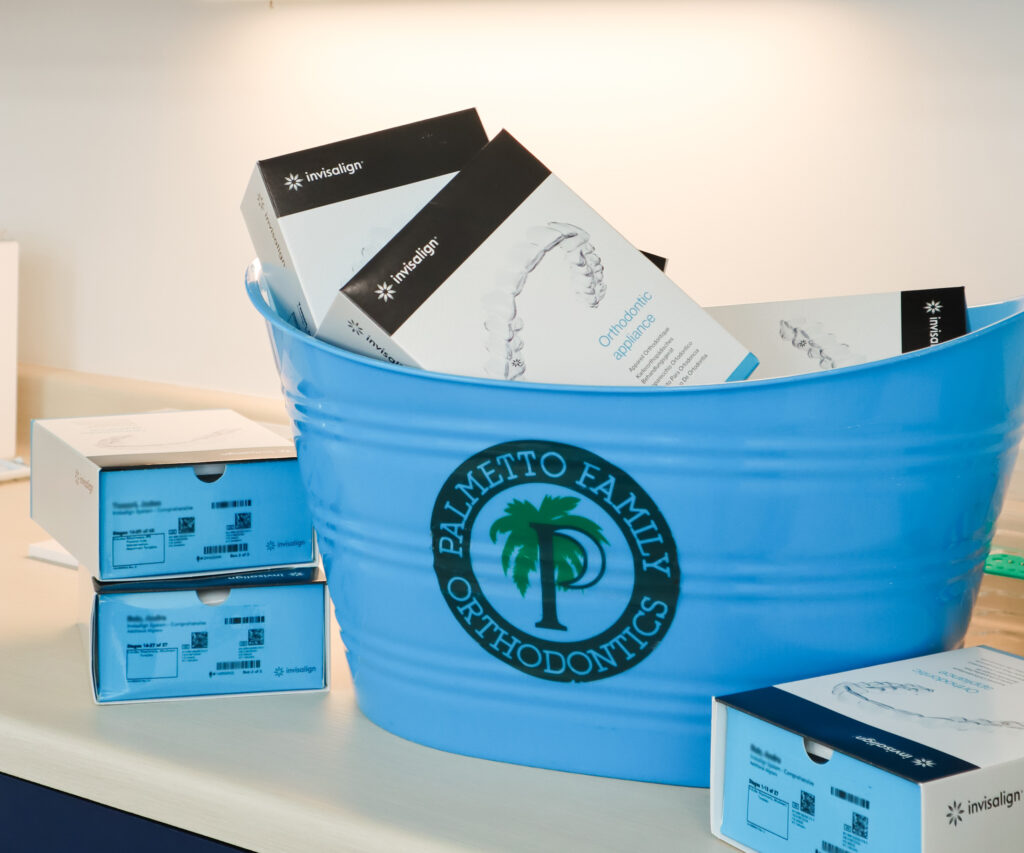 Boxes of Invisalign® clear aligners in a blue Palmetto Family Orthodontics bucket